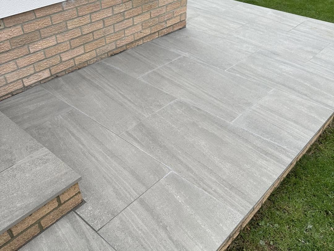 Raised porcelain patio edge on a brick plinth meeting the lawn