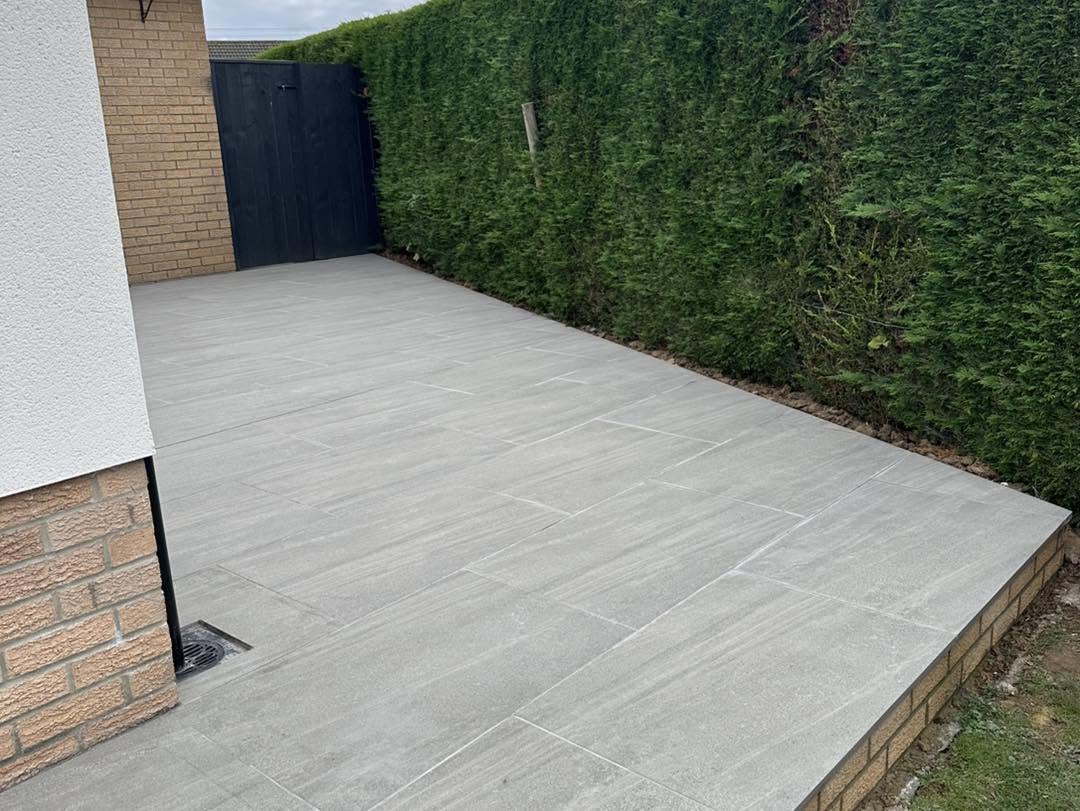 Porcelain patio running along a rendered wall beside a tall hedge