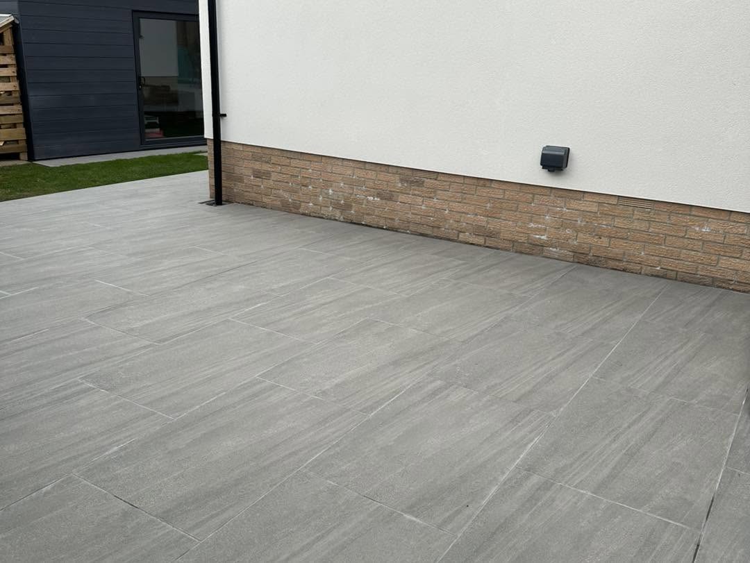 Wide grey porcelain patio along a white rendered house with brick base