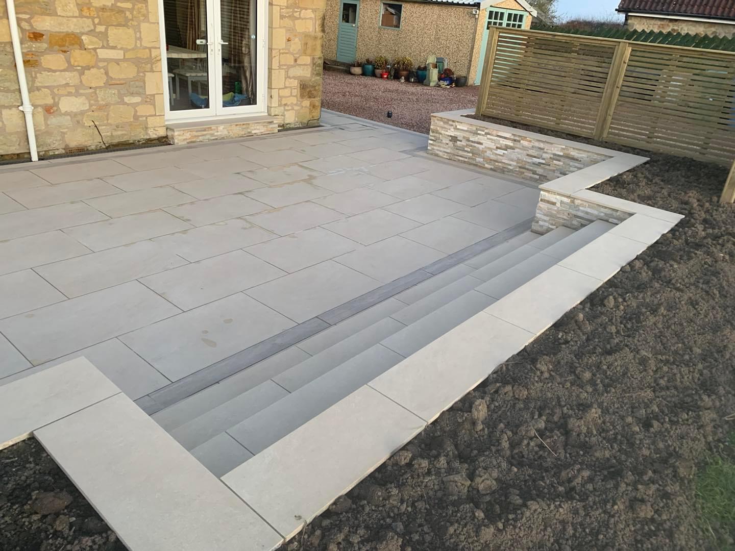 Pale grey slab patio with long, wide steps beside a sandstone house