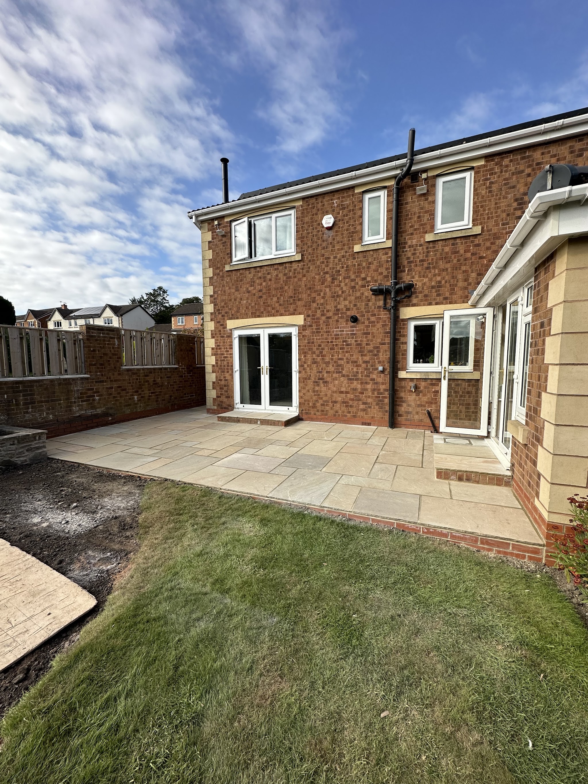 Sandstone patio laid at the back of a new brick house beside the lawn