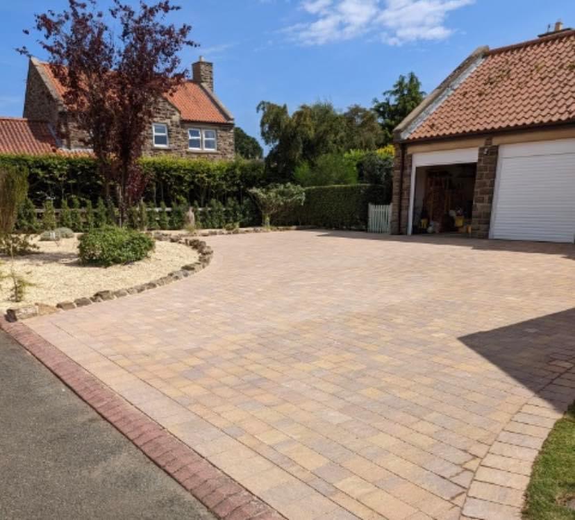 Curved buff block-paved driveway with a red border leading to a double garage