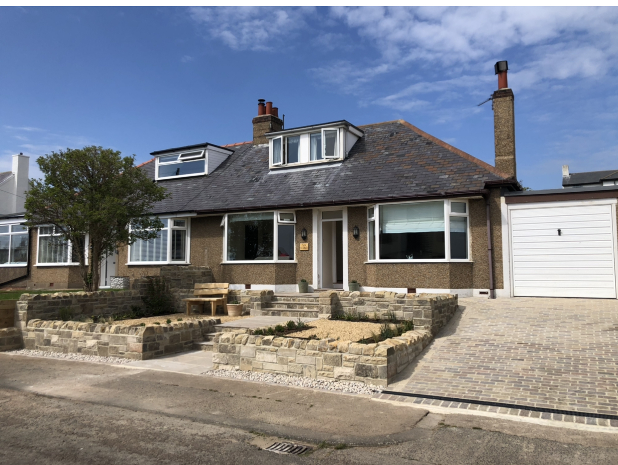 Bungalow frontage with sandstone raised beds and a block-paved drive