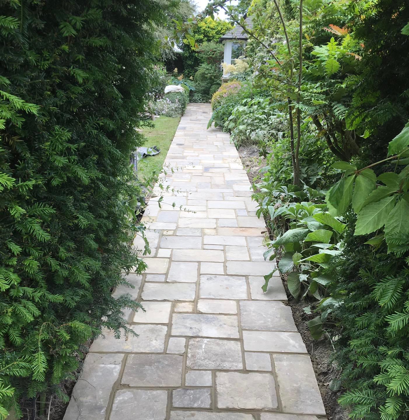 Natural stone garden path running between tall hedges and planting