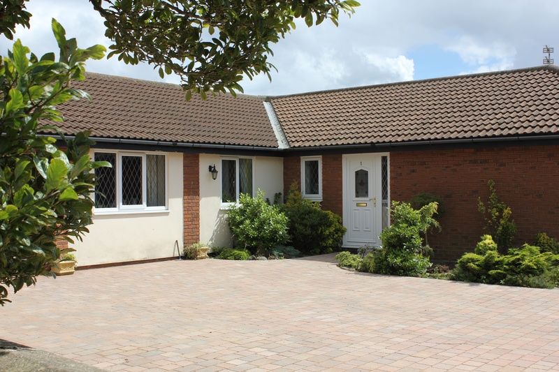 Block-paved driveway in front of a brick bungalow with shrubs