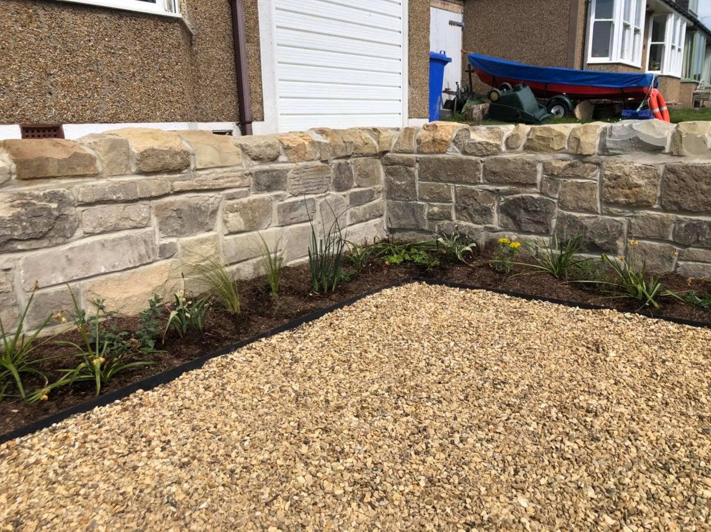 New sandstone garden wall with a gravel bed and young planting
